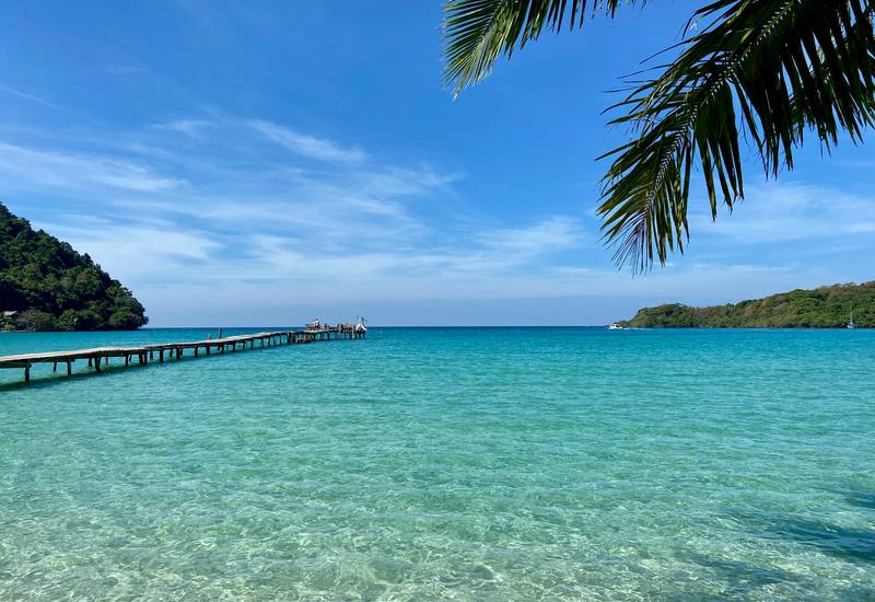 Clear turquoise water and a long wooden pier beside a green headland on Koh Kood.