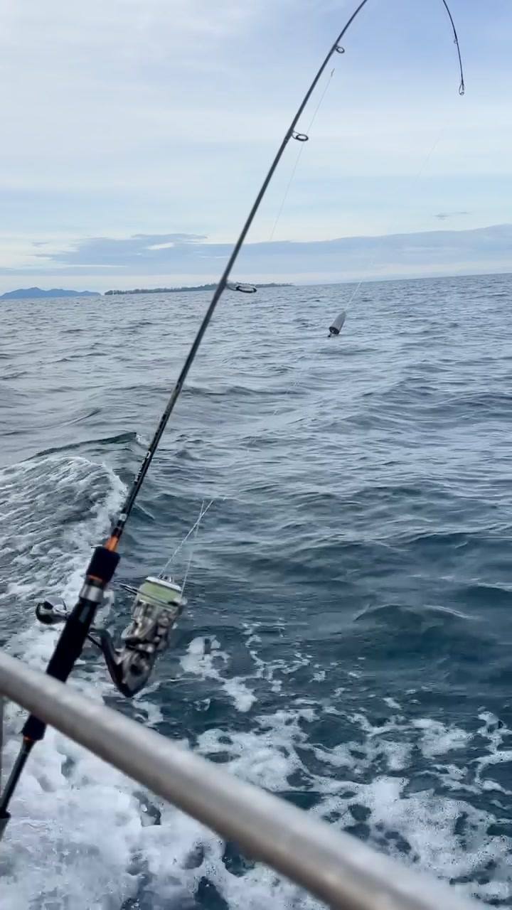 A fishing rod held over the wake of a moving boat on open sea.